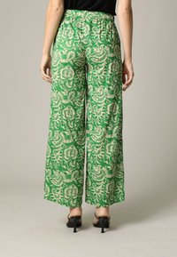 Groene wijde broek van lichte stof met een crèmekleurig bloemenpatroon. Heeft een elastische tailleband en valt soepel tot op de vloer.