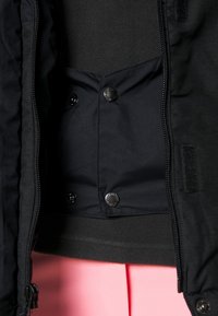 Svart jacka med en slät tygfoder inuti, knappar med tryckknapp och ett kontrasterande mjukt lager under. Inga synliga mönster eller logotyper.