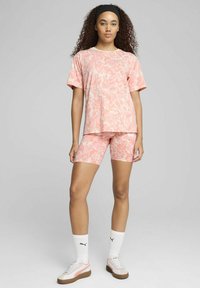 Camisa de manga corta rosa y pantalones cortos de ciclista a juego con un patrón ondulado, confeccionados en una tela suave. Combinados con calcetines blancos y zapatillas neutrales.