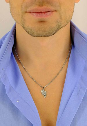 Collier en chaîne argentée avec un pendentif en forme de feuille, présentant des détails découpés complexes. Porté sur une chemise à col bleu clair.