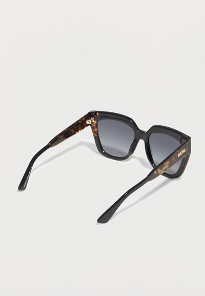 Γυαλιά ηλίου μαύρα και σε σχέδιο καβούρι με φακούς με διαβάθμιση σκούρου χρώματος και το λογότυπο «Moschino» στο δεξί πλάι, εμφανιζόμενα σε λευκό φόντο.