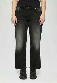 Zwarte denim wijde pijpen broek met een vervaagde afwerking, vijf zakken en zilveren hardware. G gedragen met zwarte veterschoenen.