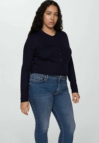 Tamno plava kardigan sa dugim rukavima i ovratnikom, u uskom kroju, uparen sa plavimfarmericama.