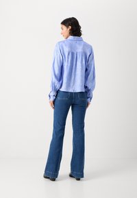 Lys blå bluse med blomstermønster, plisseret ryg og puffede ærmer, parret med mørkeblå brede jeans og sorte sko.