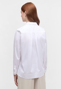 Camicia bianca a maniche lunghe con yoke sul retro, dotata di polsino con bottone e vestibilità comoda. Texture liscia e design del colletto classico.