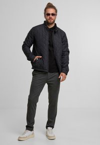 Pikowana czarna kurtka z kołnierzem stójkowym, szare spodnie i białe trampki. Zauważalne detale to zamek błyskawiczny oraz boczne kieszenie.