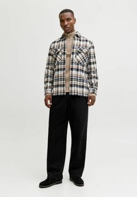 Rutet flannel skjorte i sort, hvid og beige, parret med en beige højhalset sweater og brede sorte bukser. Sykesko i sort ruskind.