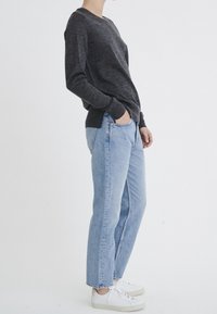 Pull en maille gris, jean droit bleu et baskets blanches. Le pull a des manches longues et un col rond. Design simple, sans motifs.