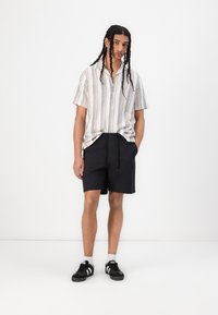 Short-sleeve, button-up shirt with multicolored vertical stripes. Paired with black shorts. Model wears black sneakers with white accents.
