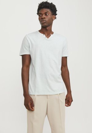 Camiseta de algodón azul claro con una ligera textura, mangas cortas y un escote en V con dos botones, combinada con pantalones beiges.