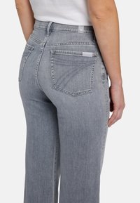 Jeans en denim gris taille haute avec une jambe droite, dotés de poches arrière et d'un léger dégradé. Détails cousus le long des poches.