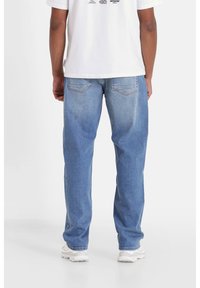 Jeans in denim blu chiaro con vestibilità rilassata, dotati di tasche posteriori e una leggera scoloritura. Abbinati a una t-shirt bianca con maniche corte.