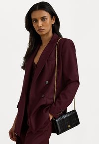 Μπορντό διπλό αμπίρ σακάκι, υφασματοποιημένο, με μια μαύρη ψεύτικη κροκοδείλια τσάντα χιαστί που διαθέτει χρυ σό αλυσίδα και λογότυπο.