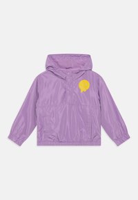 Violetti tuulenpitävä takki hupulla, jossa on keltainen hymyilevä naama -logo rinnassa ja elastiset hihansuut. Kevyt materiaali.