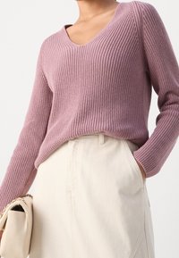 Maglione a V in tessuto rosa tenue, abbinato a una gonna beige chiaro, con vestibilità comoda e maniche lunghe.
