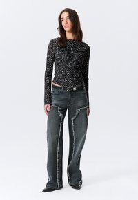 Μαύρο εφαρμοστό τοπ με μακριά μανίκια και μικρές λευκές κουκκίδες· συνδυασμένο με ανοιχτό γκρι, φθαρμένο παντελόνι με φαρδύ πόδι· μαύρη ζώνη με ασημένιες λεπτομέρειες.