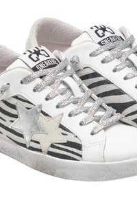 Sneakers bianchi con strisce zebra nere, applicazioni a forma di stella argentata e lacci metallici. Dettagli in pelle liscia e tessuto testurizzato.
