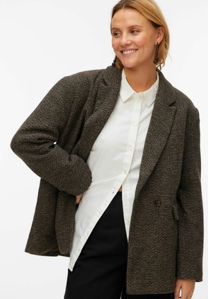 Brun tekstureret blazer med løs pasform, hakkrave og to knapper foran, båret over en hvid skjorte med knapper og sorte bukser.