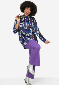 Blusa colorida y estampada en azul, púrpura y marrón con capucha, combinada con pantalones acampanados púrpuras y botas de tobillo plateadas.