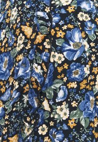Tissu sombre avec un motif floral dense comprenant de grandes fleurs bleues, blanches et jaunes avec des feuilles vertes, des boutons noirs et des coutures visibles.