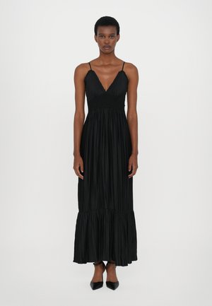 Robe maxi plissée noire avec un décolleté en V, taille smockée élastique et ourlet en couches. Accompagnée de talons noirs pointus.