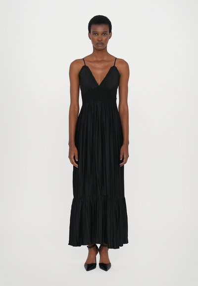 Robe maxi plissée noire avec un décolleté en V, taille smockée élastique et ourlet en couches. Accompagnée de talons noirs pointus.