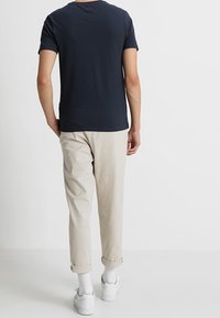 Námornická polokošile z bavlny s krátkým rukávem, spárovaná se světle béžovými zkrácenými kalhotami. Bílé tenisky s šedými akcenty dokončují outfit.