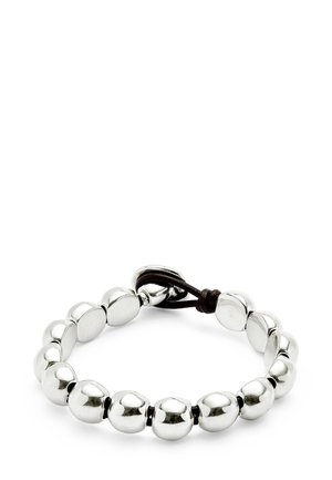 Pulsera metálica plateada con cuentas redondeadas, alternando formas suaves y ligeramente aplanadas, asegurada con un cordón marrón oscuro.