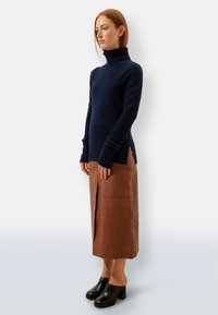 Granatowy sweter z golfem, dzianinowy, z długimi rękawami, w zestawieniu z brązową skórzaną spódnicą z bocznym rozcięciem, noszony z czarnymi klamrami na słupku.