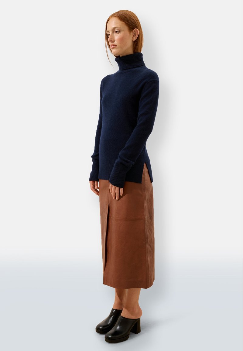 Granatowy sweter z golfem, dzianinowy, z długimi rękawami, w zestawieniu z brązową skórzaną spódnicą z bocznym rozcięciem, noszony z czarnymi klamrami na słupku.