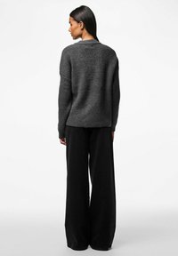 Pilkos rausvos megztinis su raukšlėta tekstūra, laisva forma, plačiu iškirpimu ir nuleistomis petnešomis, derinamas su juodomis plačiomis kelnėmis.