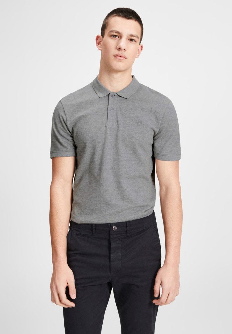 Grau Kurzarm-Polohemd mit Kragen, ausgestattet mit einem kleinen Logo auf der Brust, kombiniert mit dunklen Hosen. Glatte Textur, lässiges Design.