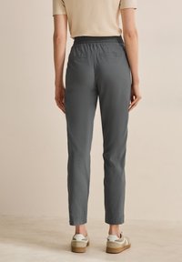 Pantalons gris, légers, fuselés avec une taille élastique, deux poches arrière et ourlets à revers, accompagnés de baskets blanches et beiges.