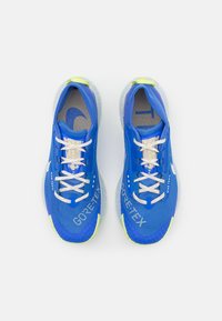 Niebieskie buty sportowe z oznaczeniem GORE-TEX, teksturowaną siateczkową cholewką, odblaskowymi akcentami oraz jasnymi sznurowadłami. Żywe zielone detale na podeszwie.