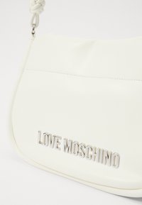 Bela torbica iz smooth umetnega usnja. Ima pleteno naramnico in kovinski napis "LOVE MOSCHINO" na sprednji strani.