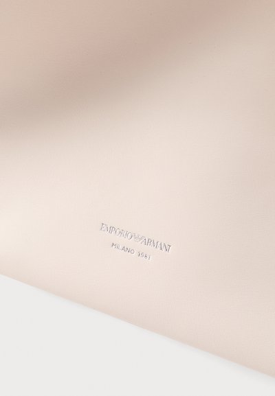 Surface en cuir beige clair embossée avec le logo Emporio Armani en argent et le texte "Milano 1981" au centre.