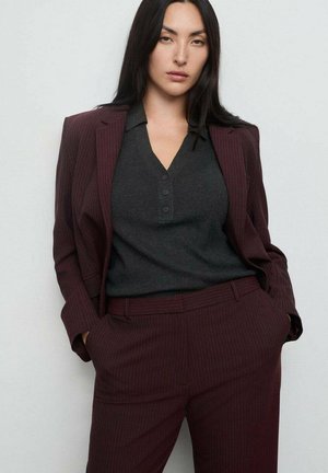 Costume bordeaux à rayures avec blazer ajusté et pantalon assorti. Chemise grise à boutons en dessous, fabriquée en tissu lisse.