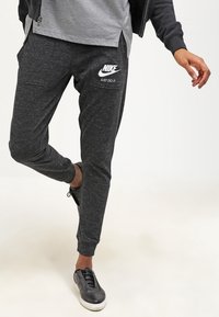 Černé tepláky s melírovaným vzorem a elastickými manžetami, s bílým logem "NIKE JUST DO IT" na stehně. Vyrobeno z měkkého a elastického materiálu.