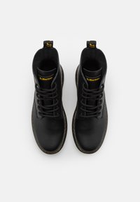 Black leather ankle boots with round toes and sturdy laces, featuring a yellow logo on the tongue and a contrasting outsole stitching.