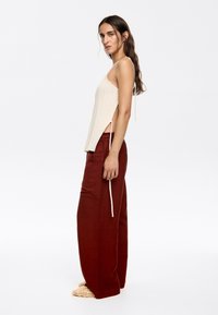 Cream knit tank top with side slits, paired with high-waisted, wide-leg burgundy pants featuring a drawstring and textured fabric.