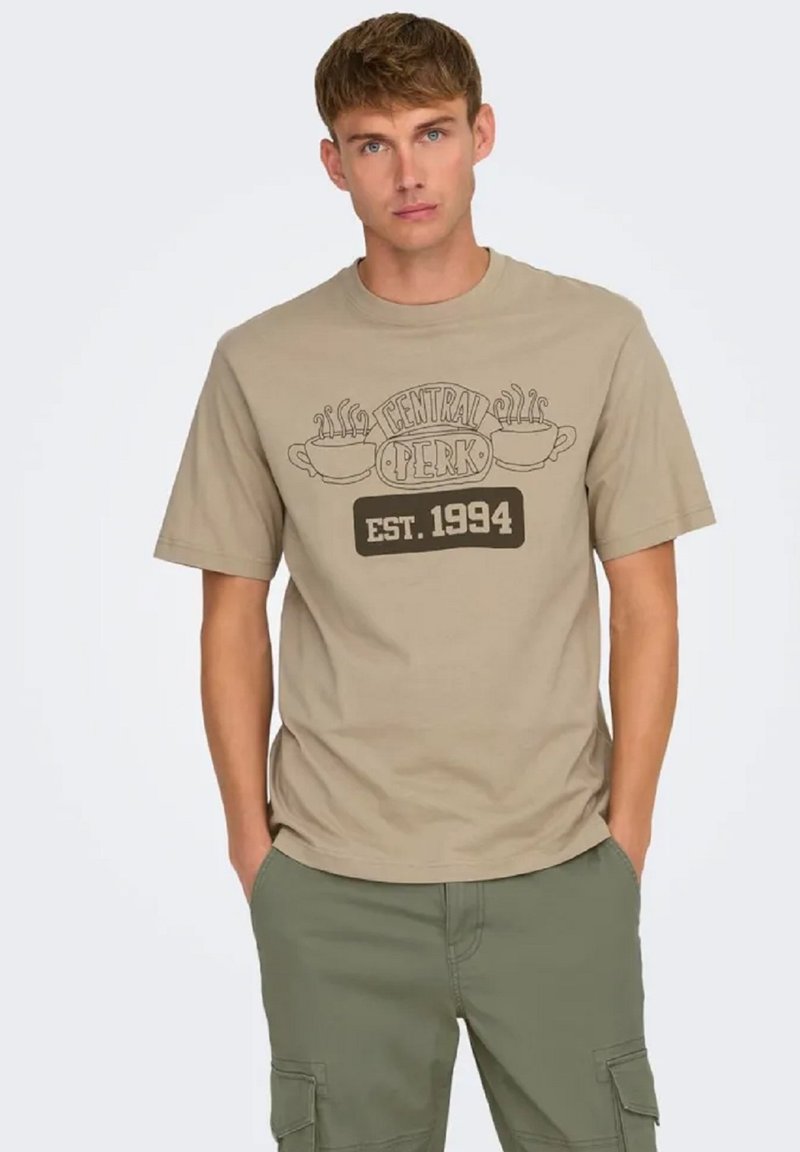 Camiseta de algodón beige con un gráfico de Central Perk en marrón que incluye dos tazas de café y el texto "EST. 1994", combinada con pantalones cortos de cargador en verde oliva.