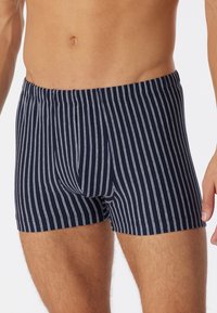 Boxer in blu navy con strisce verticali bianche, vita elasticizzata e una texture morbida. Il design è aderente e moderno.