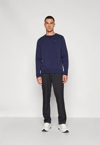 Námořnická mikina s kulatým výstřihem a logem; v kombinaci s tmavými kalhotami a bílými teniskami. Jednoduchý design, texturovaná látka, pohodlný střih.