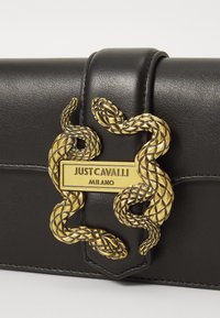 Black leather clutch featuring a gold snake motif and logo plate. Detailed stitching and textured snake design accentuate the front.