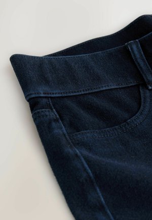 Donkerblauwe spijkerbroek van denim met een brede tailleband, voorzien van een voorzak en zichtbare stiksels langs de randen. Over het algemeen een gladde textuur.