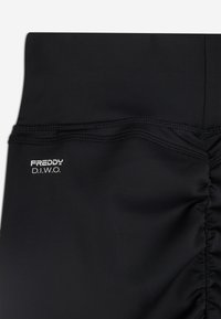 Leggings neri realizzati in materiale elasticizzato con dettagli arricciati sui lati e un piccolo logo bianco "FREDDY D.I.W.O." sulla vita.