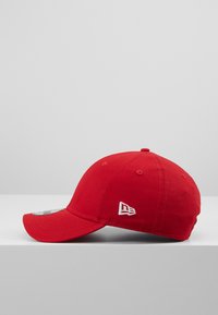 Piros baseball sapka, pamutból készült, ívelt karimával, hat szellőzőnyílással és egy fehér hímzett logóval az oldalon.