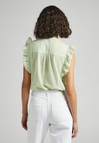 Jasnozielony top bez rękawów z falbaniastymi ramionami, szwem yoke na plecach i miękką teksturą, w połączeniu z białymi spodniami o wysokim stan.