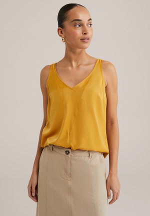 Yellow satin tank top with a v-neck design and thin straps, layered over a beige buttoned skirt, creating a casual outfit.