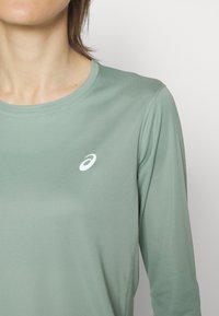 Langärmliges Sportoberteil in Mintgrün, aus glattem, leichtem Material mit einem runden Ausschnitt und kleinem, weißem Logo auf der Brust.